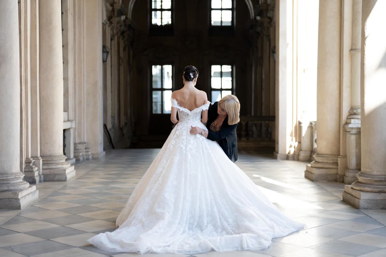 Una consulente dell'atelier sistema l'abito addosso a una sposa sotto un porticato