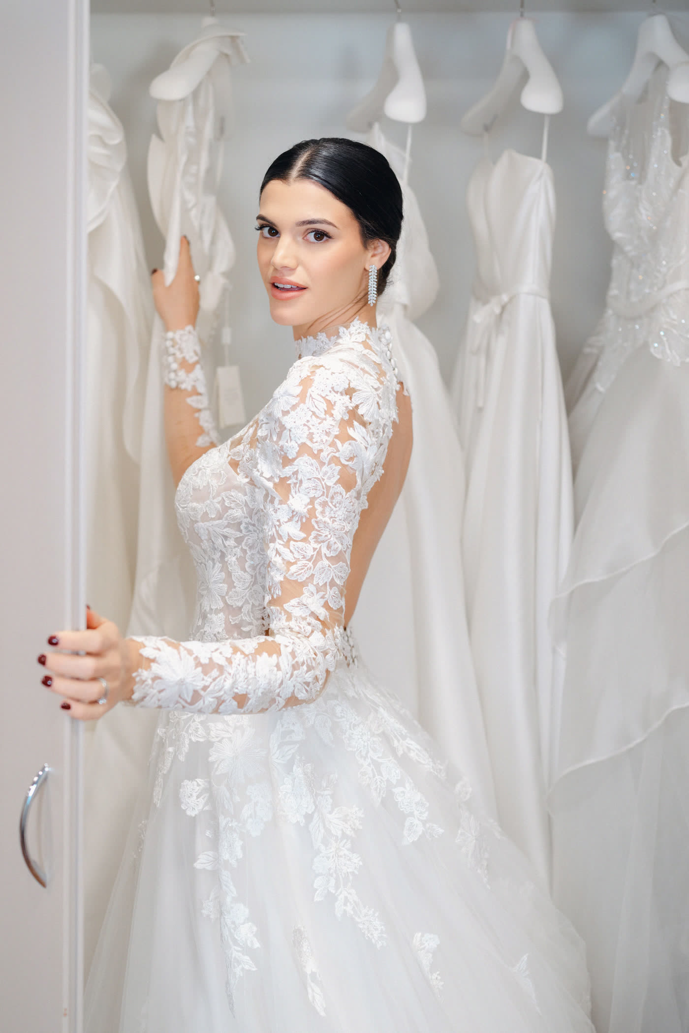 Sposa con abito in pizzo a maniche lunghe tra gli abiti dell'atelier